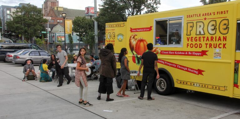 Volunteers serving meals from the free food truck to people waiting on the sidewalk